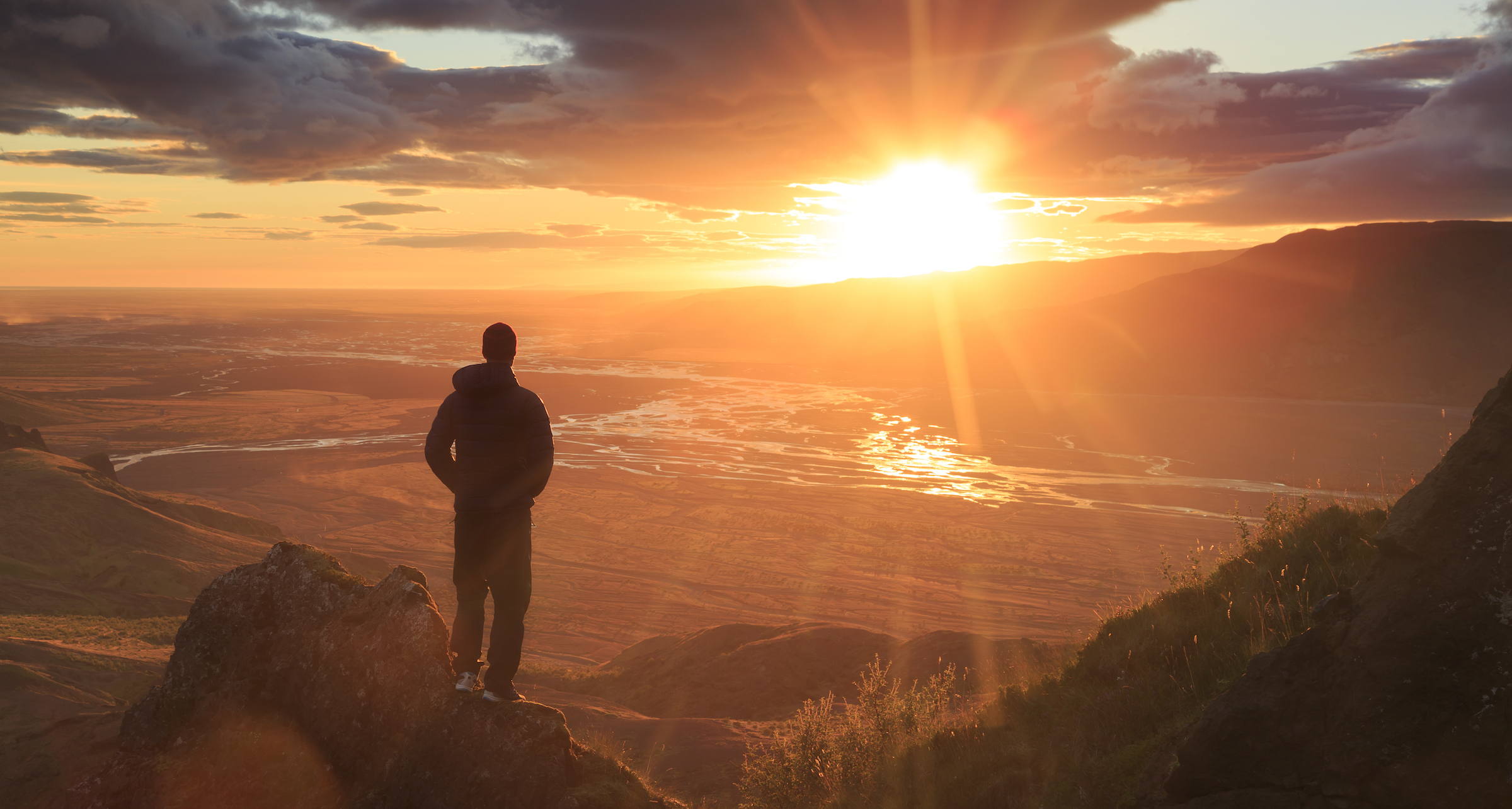 Man standing on a ledge of a mountain, enjoying the sunset over a river valley in Thorsmork, Iceland. With lens flare.
